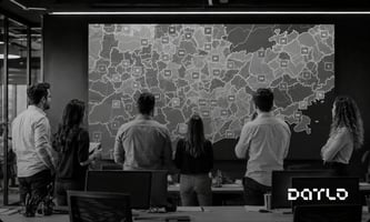 Equipe comercial de costas diante de um grande painel com o mapa de uma região do Brasil coberto por marcadores de empresas, com áreas cheias e áreas vazias, representando a cobertura de mercado de uma operação B2B