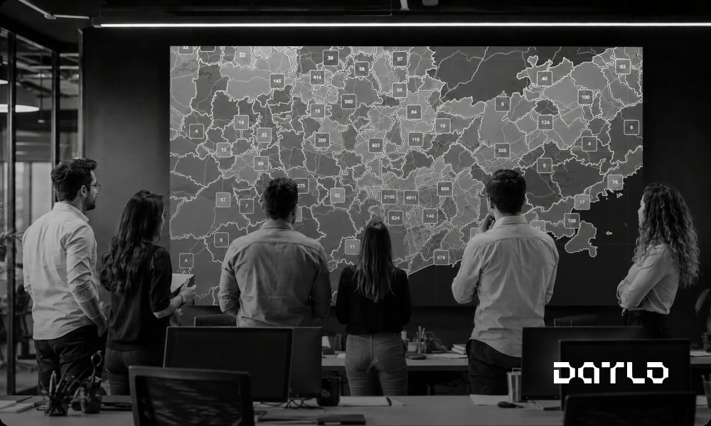 Equipe comercial de costas diante de um grande painel com o mapa de uma região do Brasil coberto por marcadores de empresas, com áreas cheias e áreas vazias, representando a cobertura de mercado de uma operação B2B